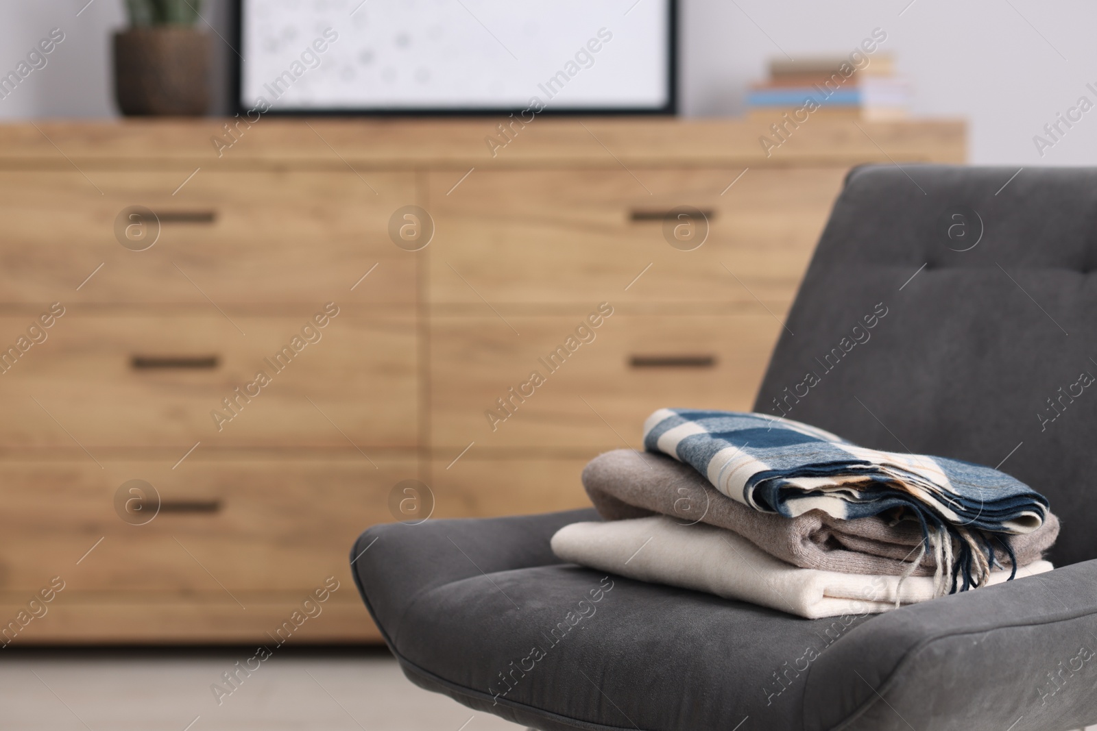 Folded wool sweaters and scarf on armchair indoors, space for text Photo of Folded wool sweaters and scarf on armchair indoors, space for text