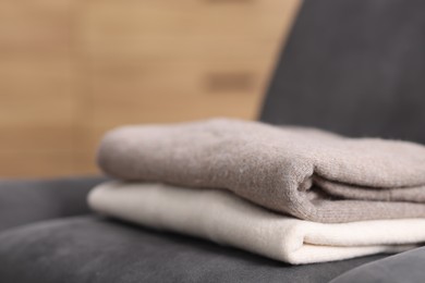 Photo of Folded wool sweaters on armchair indoors, closeup