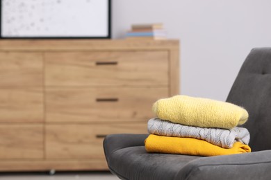 Photo of Stack of wool sweaters on armchair indoors, space for text