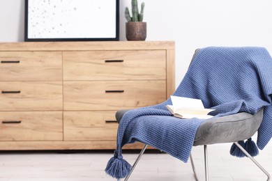 Photo of Wool blanket and open book on armchair indoors