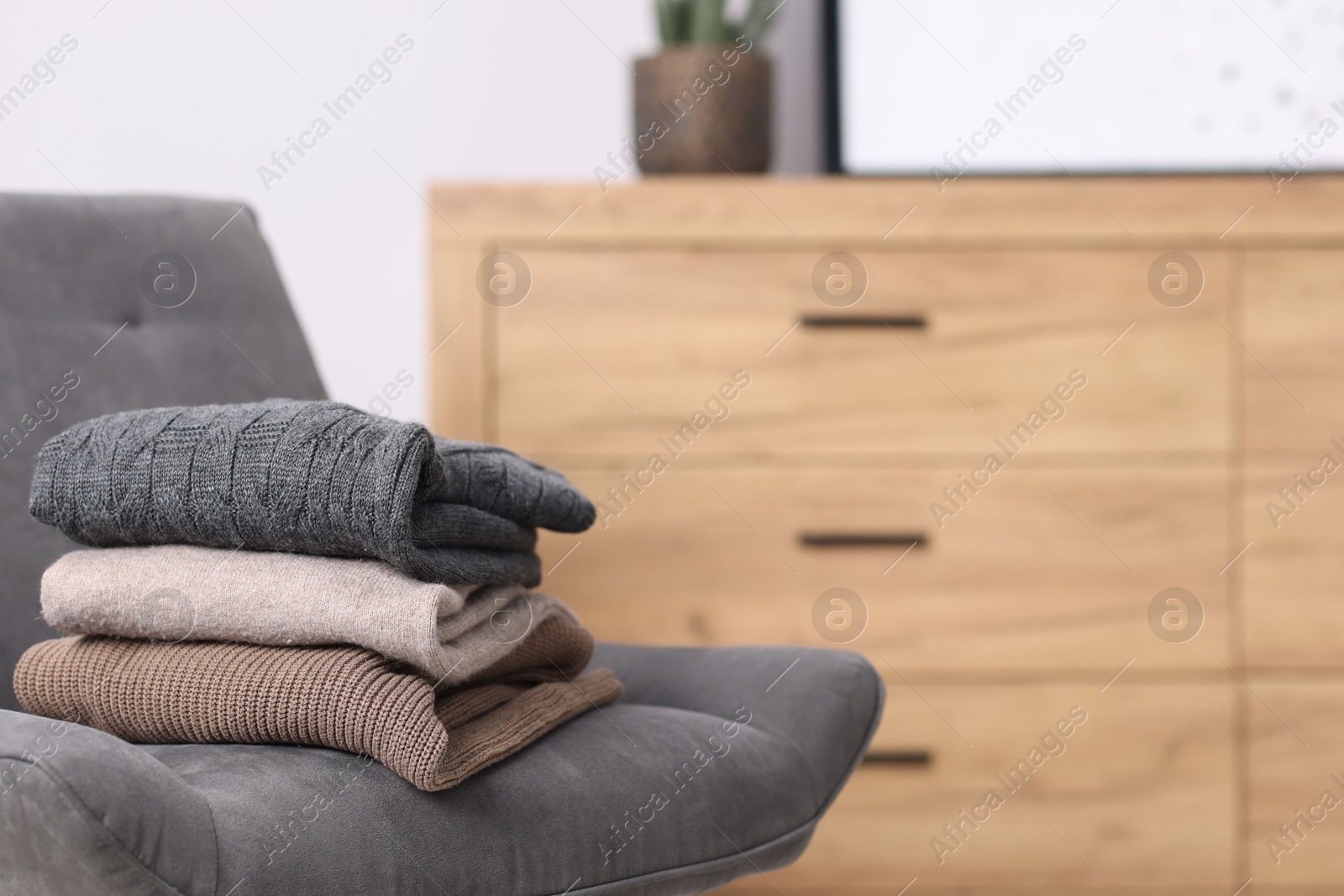 Folded wool sweaters on armchair indoors, space for text Photo of Folded wool sweaters on armchair indoors, space for text