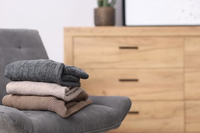 Photo of Folded wool sweaters on armchair indoors, space for text