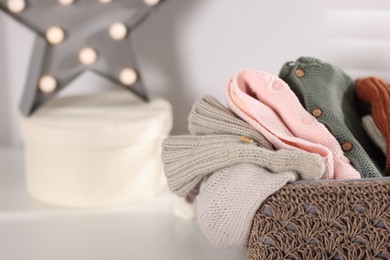 Photo of Wool baby clothes in basket on white table indoors, closeup