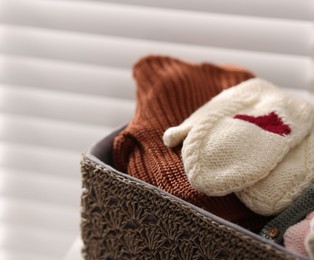 Photo of Wool baby clothes and mittens in basket on light background, closeup
