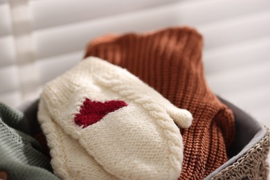 Photo of Wool baby clothes and mittens in basket on light background, closeup