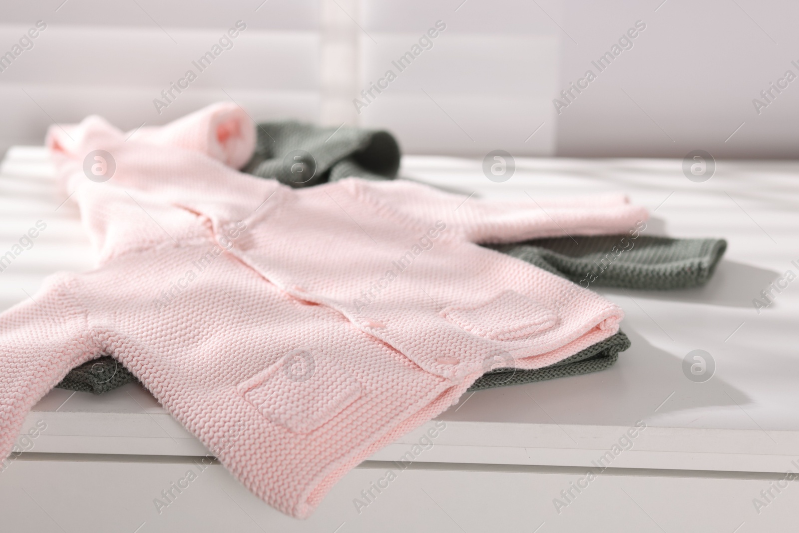 Photo of Wool baby sweaters on white nightstand indoors, closeup