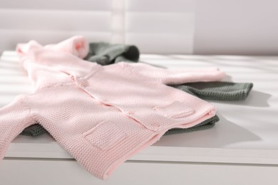 Photo of Wool baby sweaters on white nightstand indoors, closeup