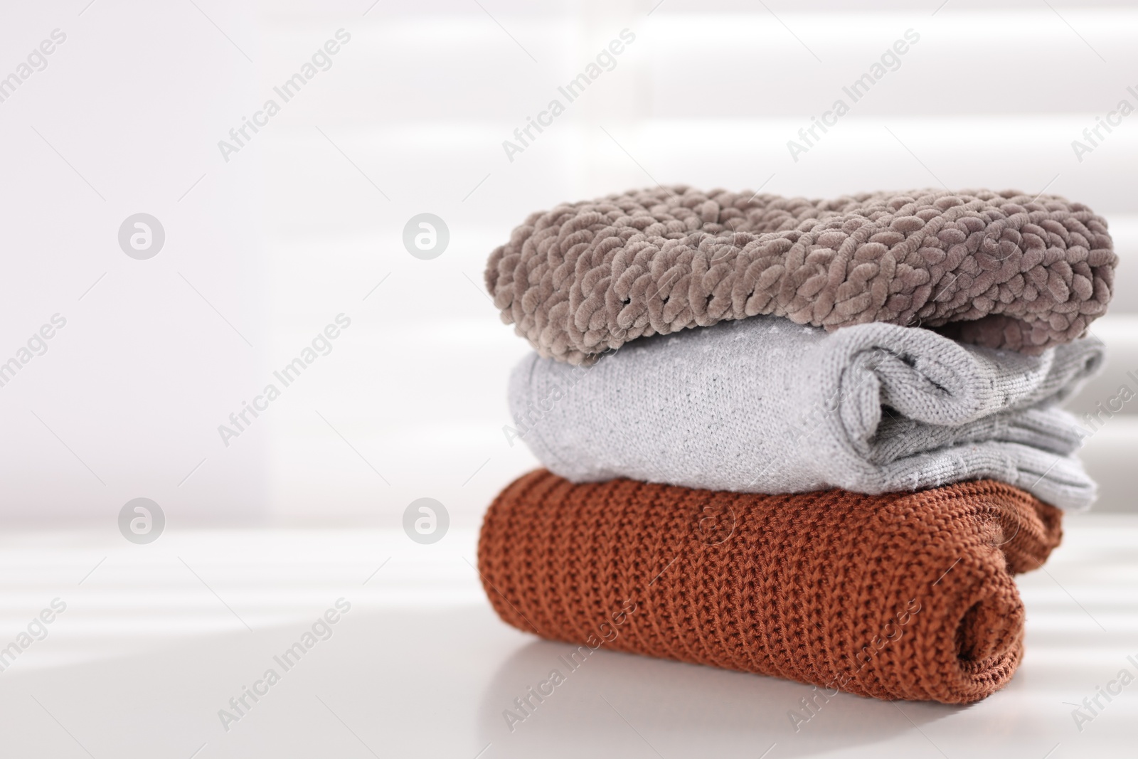 Stack of wool baby clothes on white table indoors, space for text Photo of Stack of wool baby clothes on white table indoors, space for text