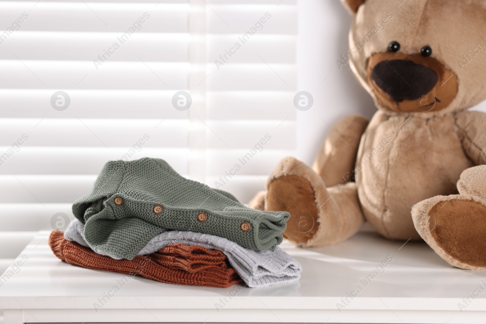 Wool baby clothes and teddy bear on white table indoors Photo of Wool baby clothes and teddy bear on white table indoors