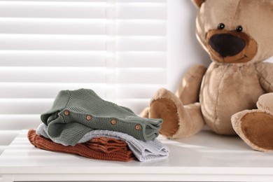 Photo of Wool baby clothes and teddy bear on white table indoors