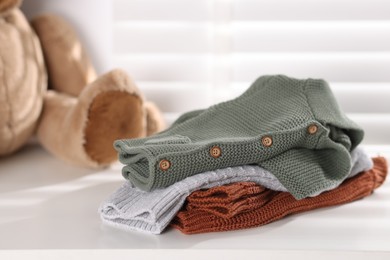 Photo of Wool baby clothes and teddy bear on white table indoors, closeup
