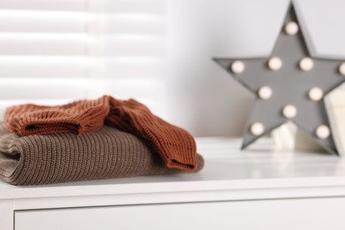 Photo of Wool sweaters and star shaped lamp on white nightstand indoors