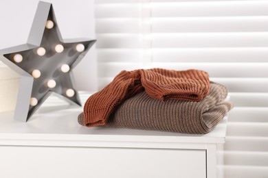 Photo of Wool sweaters and star shaped lamp on white nightstand indoors