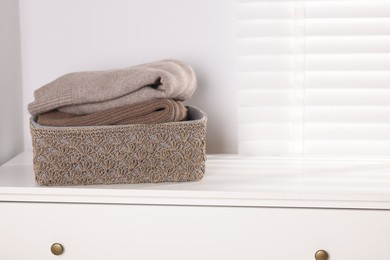 Photo of Wool sweaters in basket on white nightstand indoors, space for text