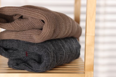 Photo of Folded wool sweaters on wooden shelf indoors, closeup