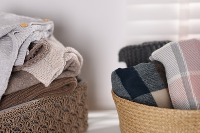 Photo of Wool sweaters and scarves in baskets on table indoors, closeup