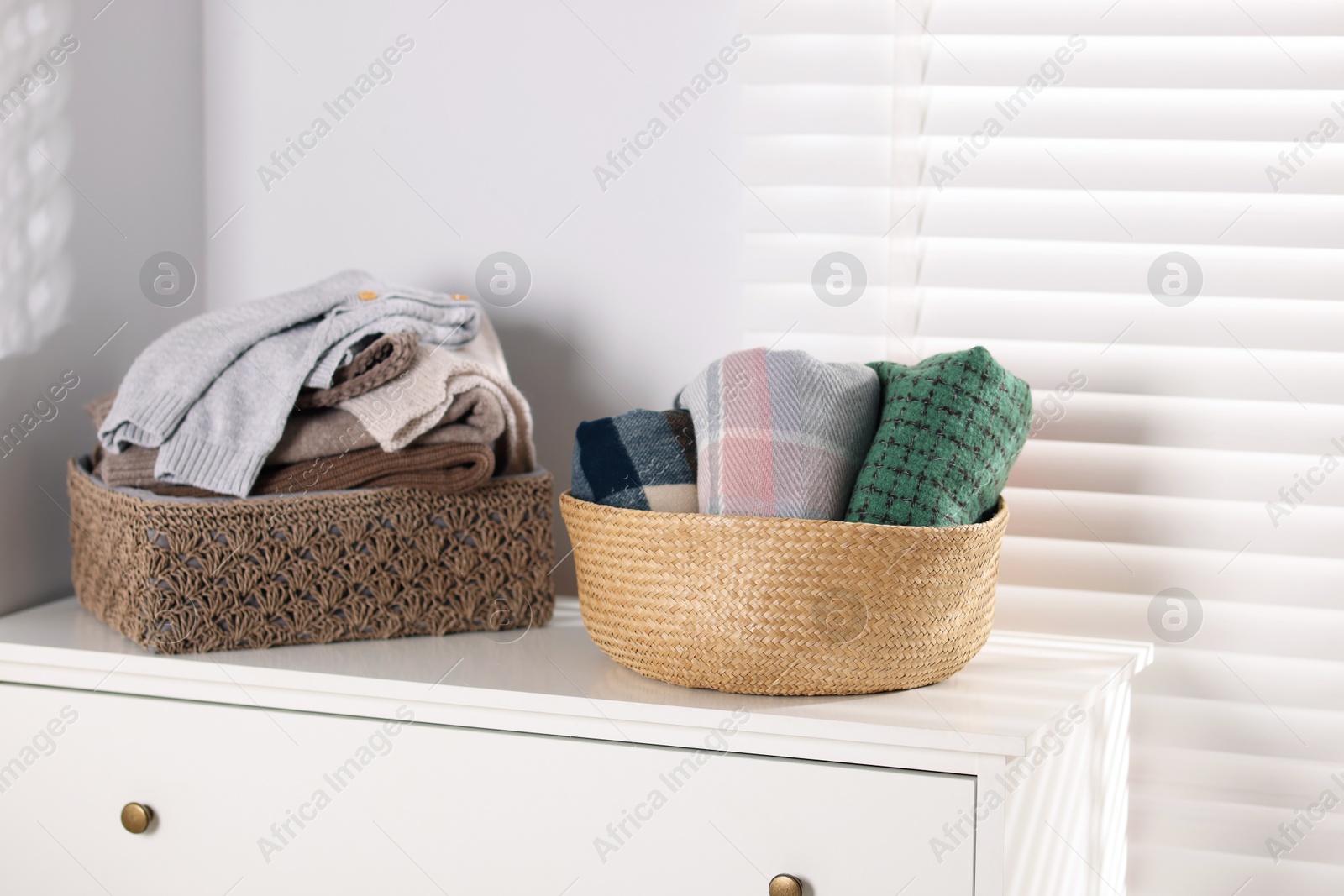 Wool sweaters and scarves in baskets on white nightstand indoors Photo of Wool sweaters and scarves in baskets on white nightstand indoors