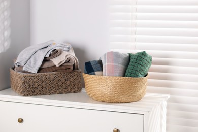 Photo of Wool sweaters and scarves in baskets on white nightstand indoors