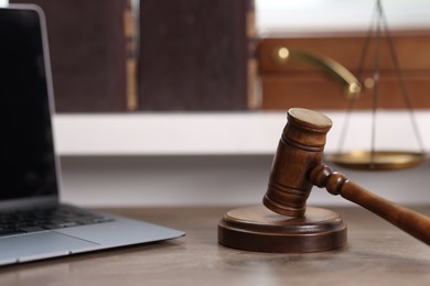 Photo of Judge. Laptop, gavel and scales on wooden table in office, selective focus