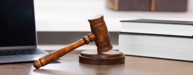 Photo of Judge. Laptop, gavel and books on wooden table in office, closeup