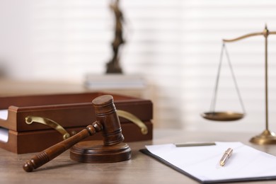 Photo of Judge. Gavel, scales, clipboard and pen on wooden table in office, selective focus