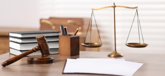 Photo of Judge. Gavel, scales, books, papers and pens on wooden table in office
