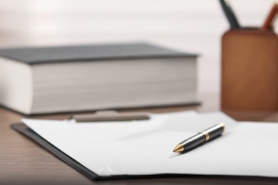 Photo of Judge. Clipboard with papers, pen and book on wooden table in office, closeup