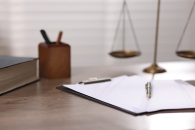 Photo of Judge. Scales, book, papers and pen on wooden table in office, closeup