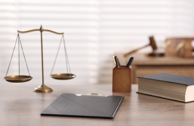 Photo of Judge. Scales, book, clipboard and pens on wooden table in office, selective focus