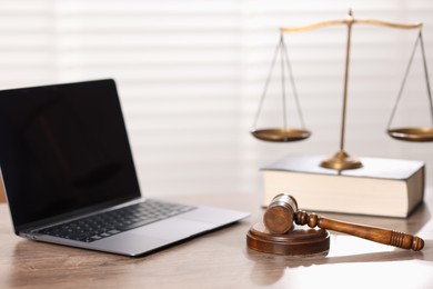 Photo of Judge. Laptop, gavel, scales and book on wooden table in office, selective focus