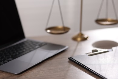 Photo of Judge. Laptop, scales and clipboard on wooden table in office, closeup