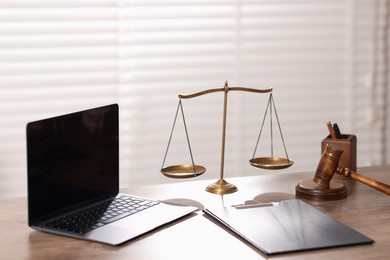 Photo of Judge. Laptop, gavel, scales and clipboard on wooden table in office