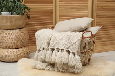 Photo of Woolen blankets and pillows in basket on floor indoors