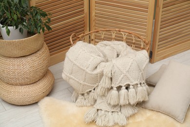 Photo of Woolen blanket in basket and pillows on floor indoors, above view