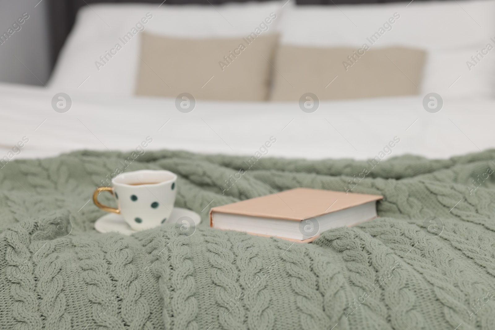 Woolen blanket, cup of drink and book on bed indoors, closeup Photo of Woolen blanket, cup of drink and book on bed indoors, closeup
