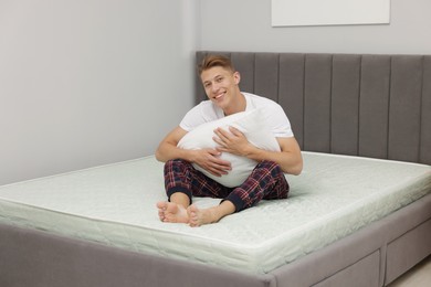 Photo of Happy man with pillow sitting on soft mattress at home
