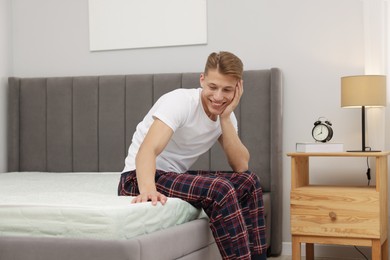 Photo of Man touching soft mattress on bed at home