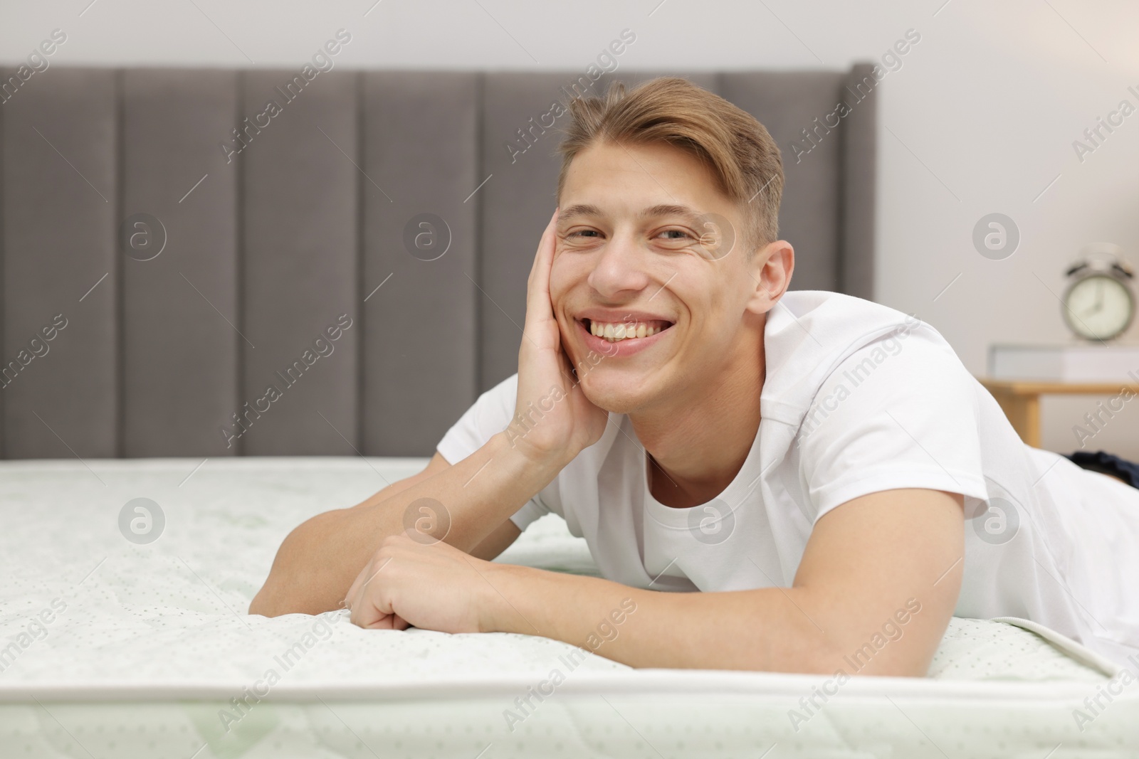 Happy man near bed with soft mattress indoors, space for text Photo of Happy man near bed with soft mattress indoors, space for text