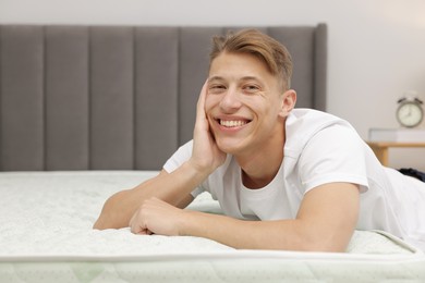 Photo of Happy man near bed with soft mattress indoors, space for text