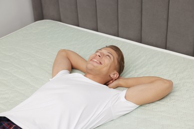 Photo of Happy man lying on soft mattress at home, above view