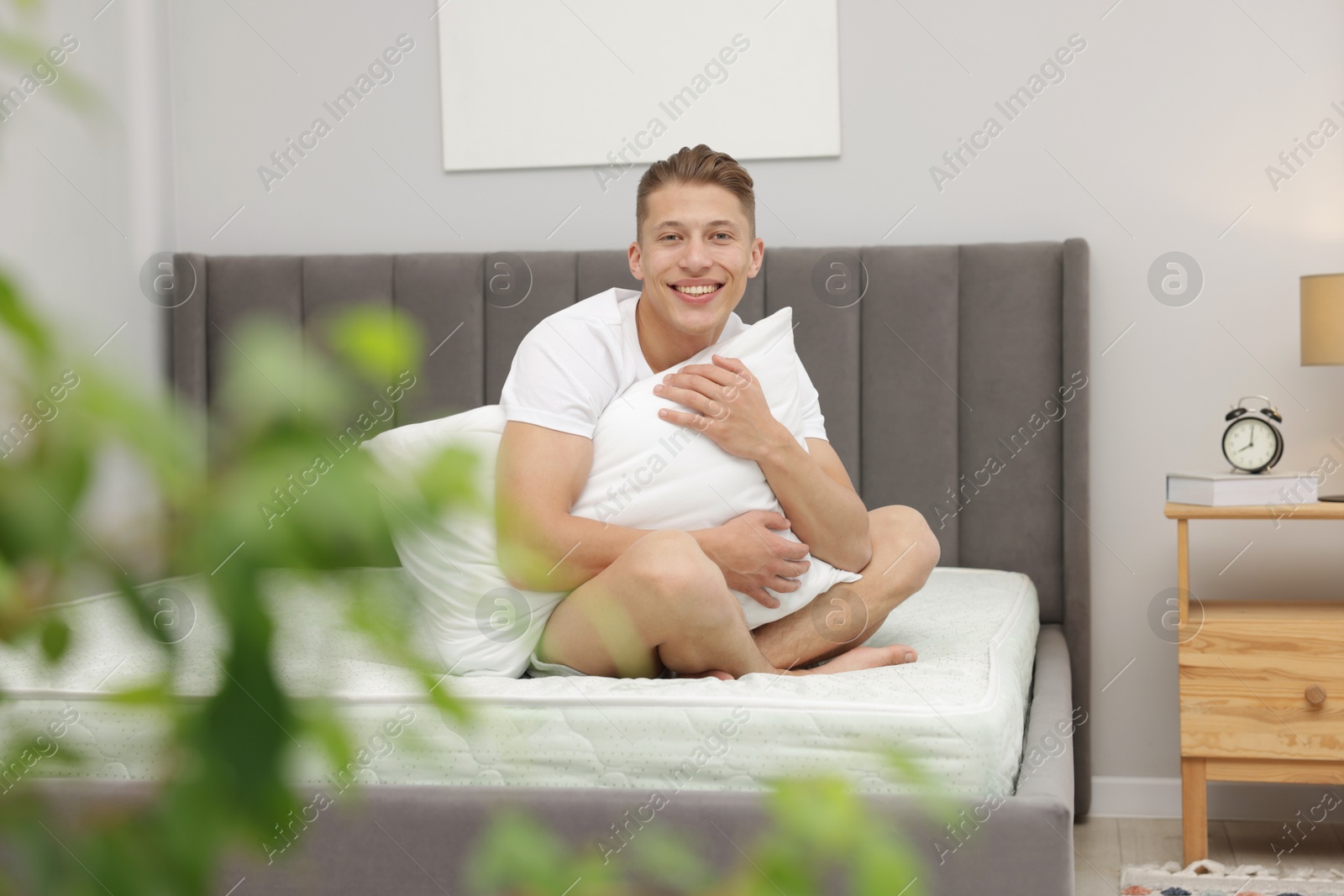 Man with pillow sitting on soft mattress at home Photo of Man with pillow sitting on soft mattress at home