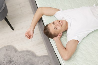 Photo of Happy man lying on soft mattress at home, above view
