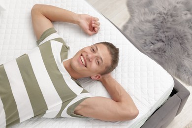 Photo of Happy man lying on soft mattress at home, top view
