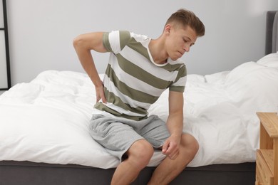 Photo of Man suffering from back pain after sleeping on uncomfortable mattress at home