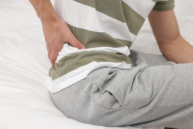Photo of Man suffering from back pain after sleeping on uncomfortable mattress at home, closeup