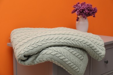 Photo of Woolen blanket and flowers on cabinet near orange wall indoors, closeup