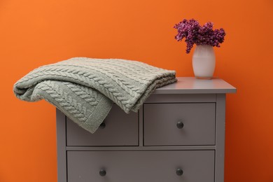 Photo of Woolen blanket and flowers on cabinet near orange wall indoors