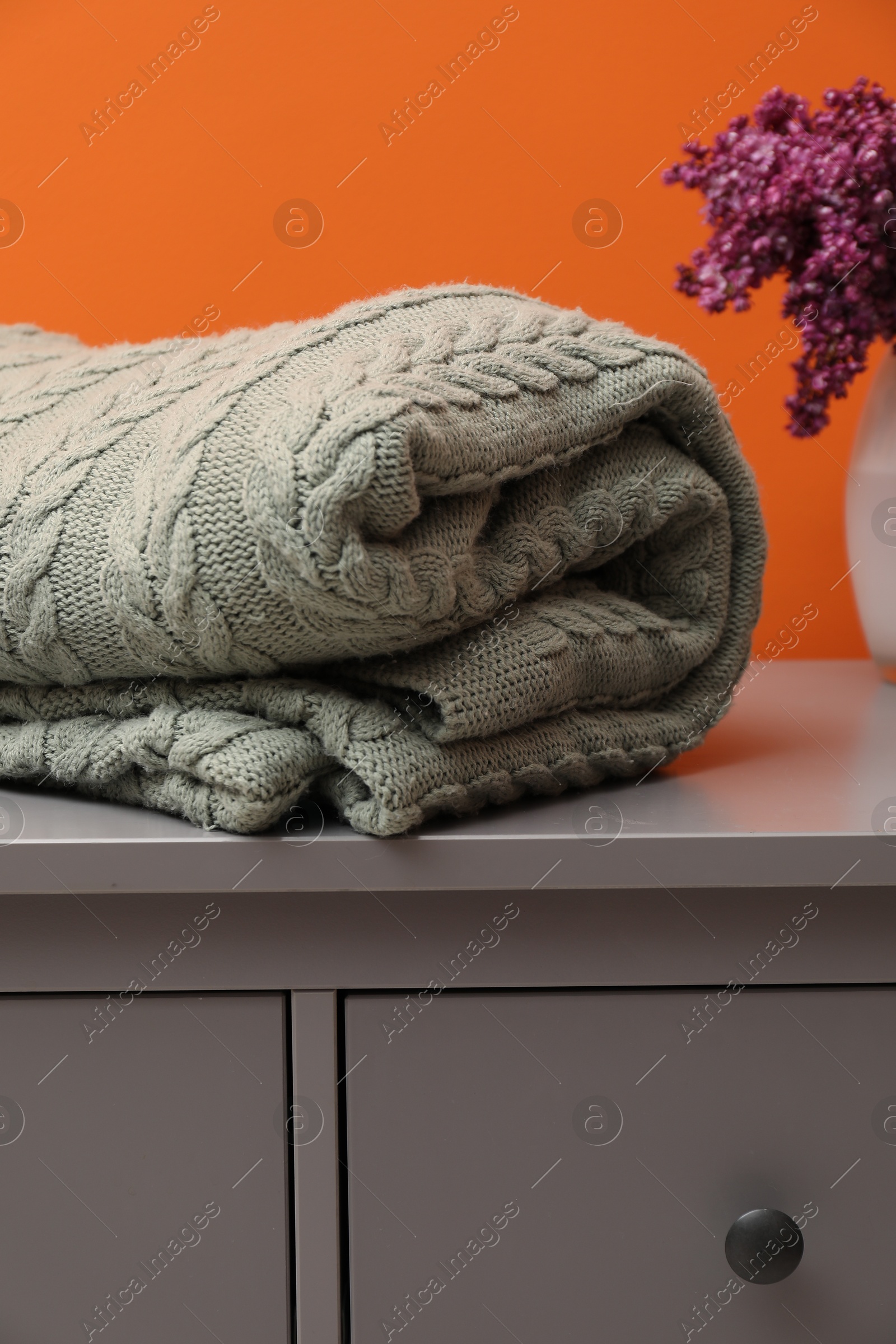 Woolen blanket and flowers on cabinet near orange wall indoors, closeup Photo of Woolen blanket and flowers on cabinet near orange wall indoors, closeup