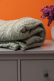Photo of Woolen blanket and flowers on cabinet near orange wall indoors, closeup