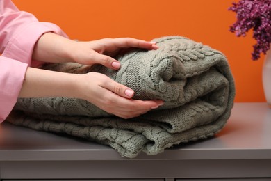 Photo of Woman with folded woolen blanket near orange wall indoors, closeup